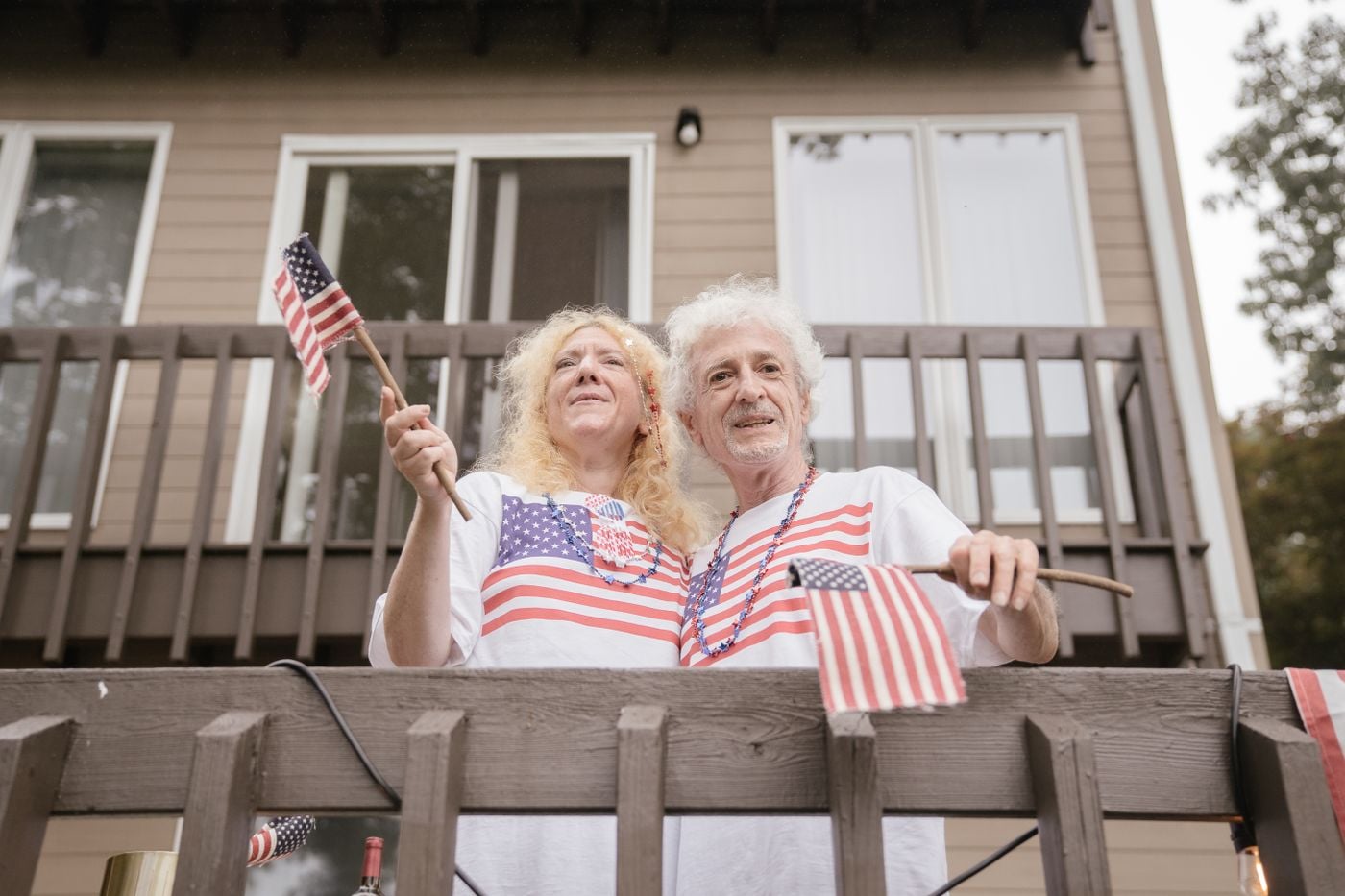Senior couple on balcony with US flags, enjoying a festive celebration outdoors.